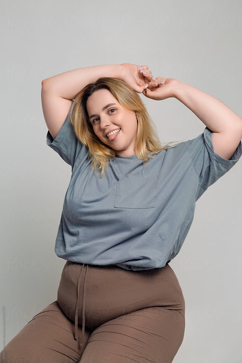 Happy young plus size woman sitting in room with gray backdrop