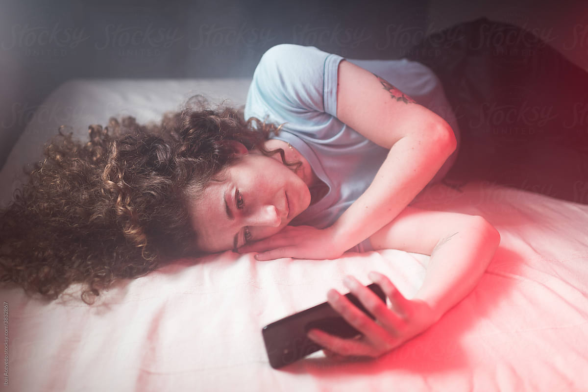Young smiling woman using phone on bed