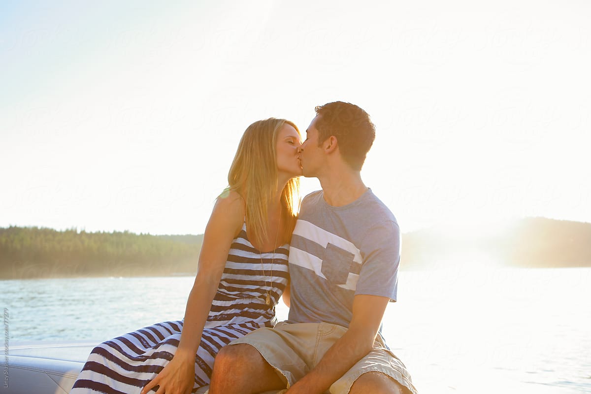 Happy couple kissing on lake at sunset
