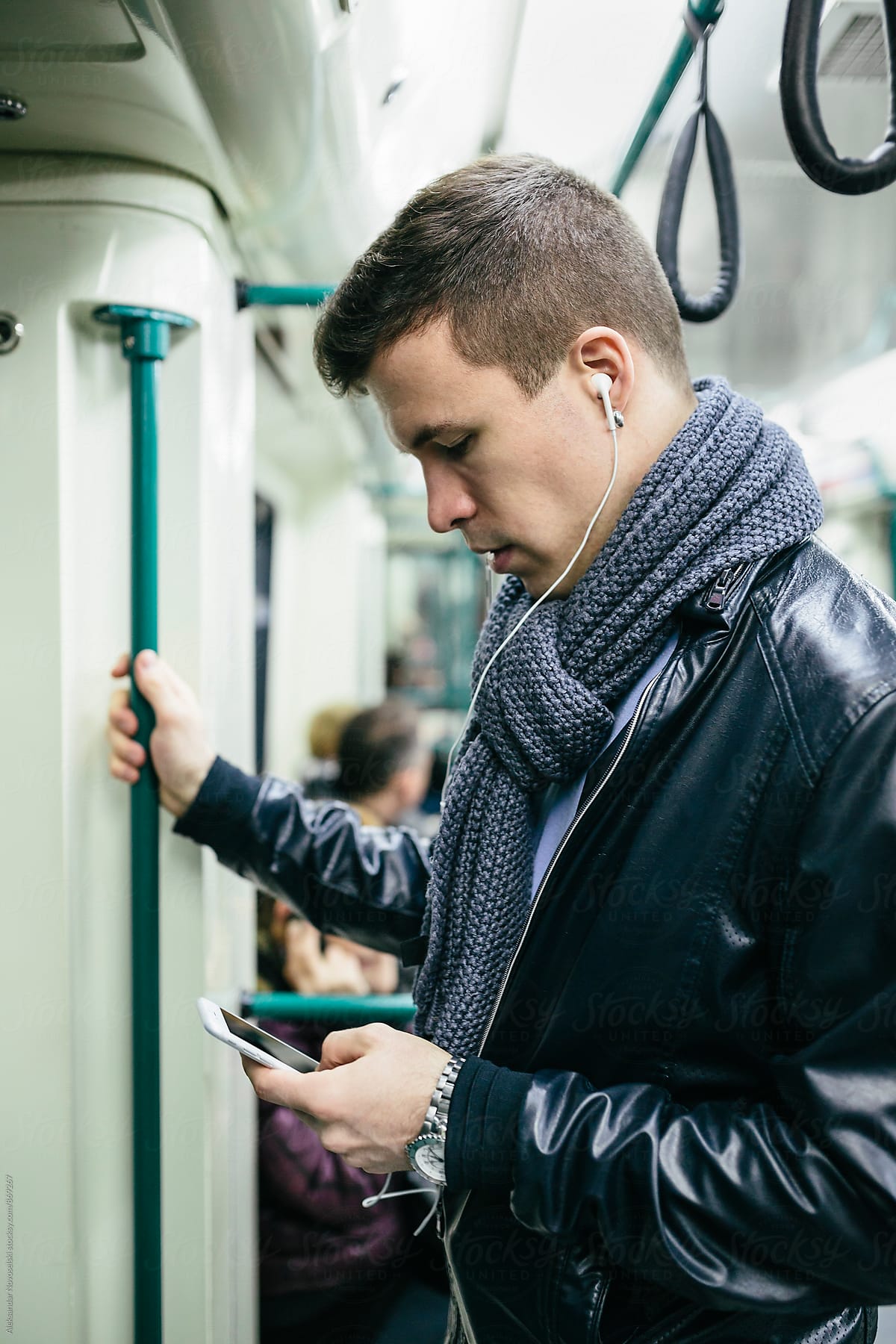 Young man using his smartphone with his headphones plugged in, in the subway