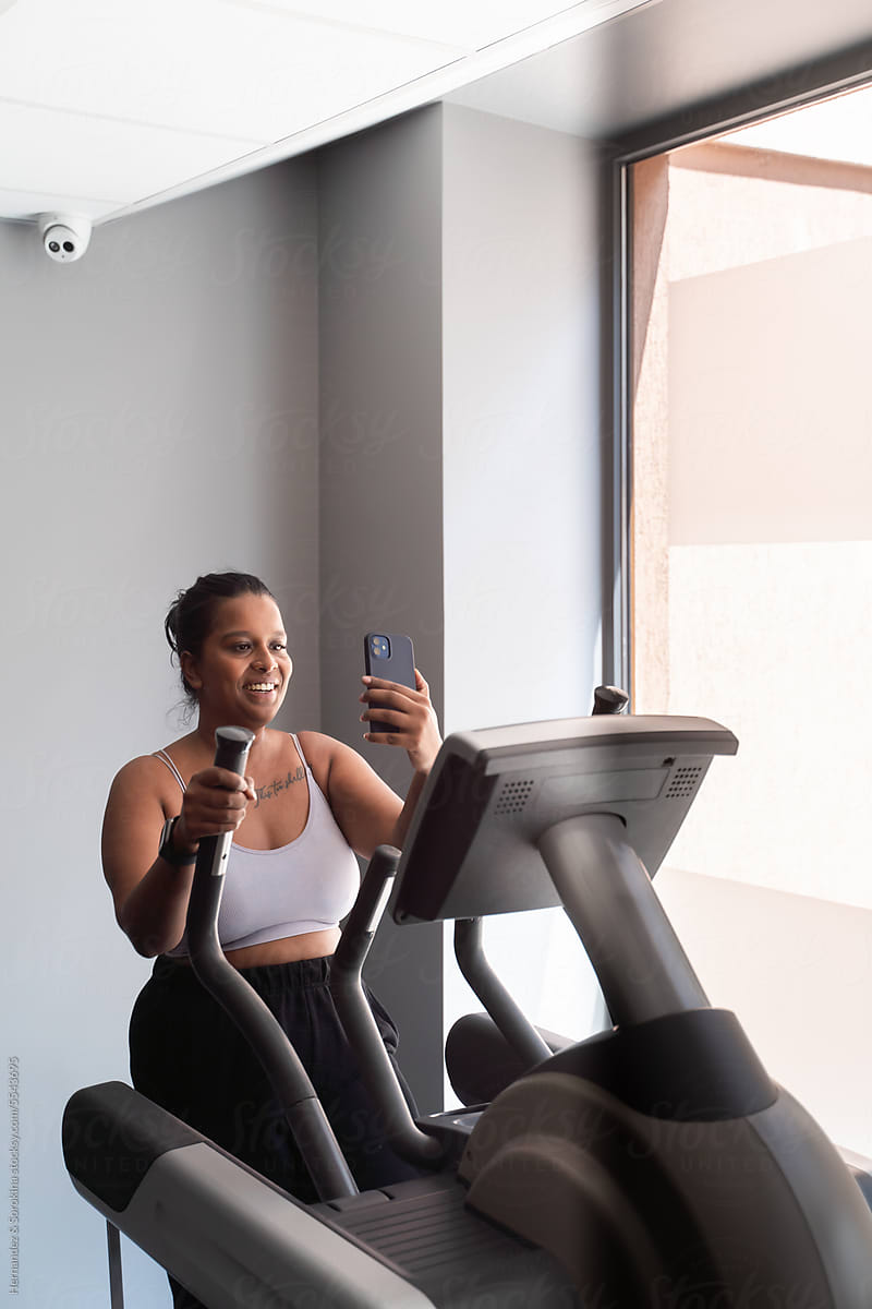 Curvy Woman Using Phone Working Out In The Gym