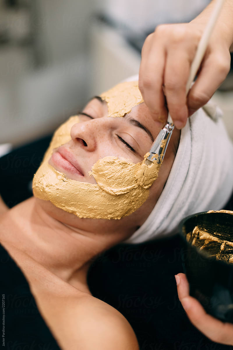 Woman applying gold mask at spa center