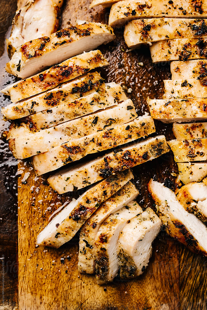 Sliced grilled herb chicken on a wooden cutting board