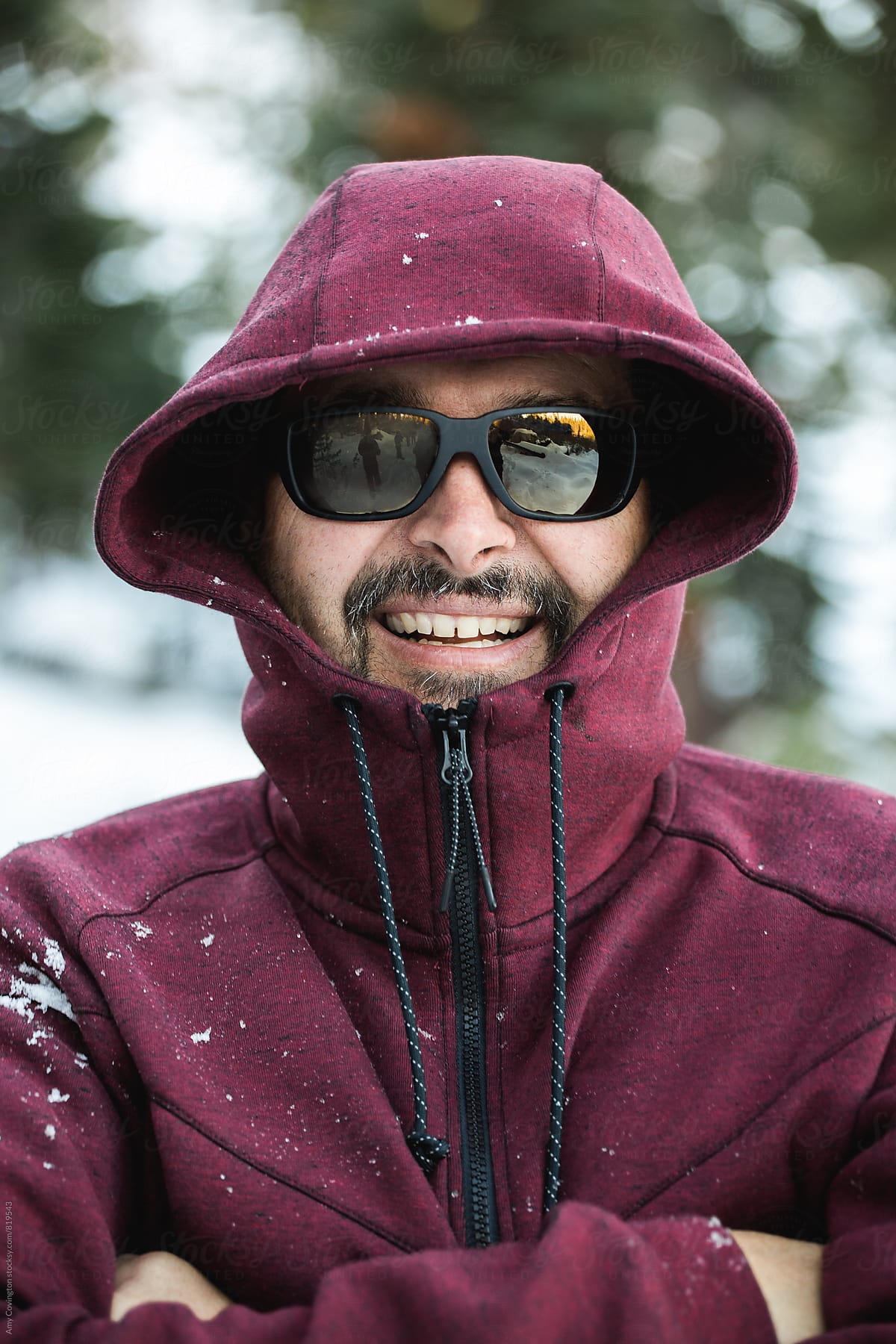 Man wearing a zipped up jacket and sunglasses smiling in the snow