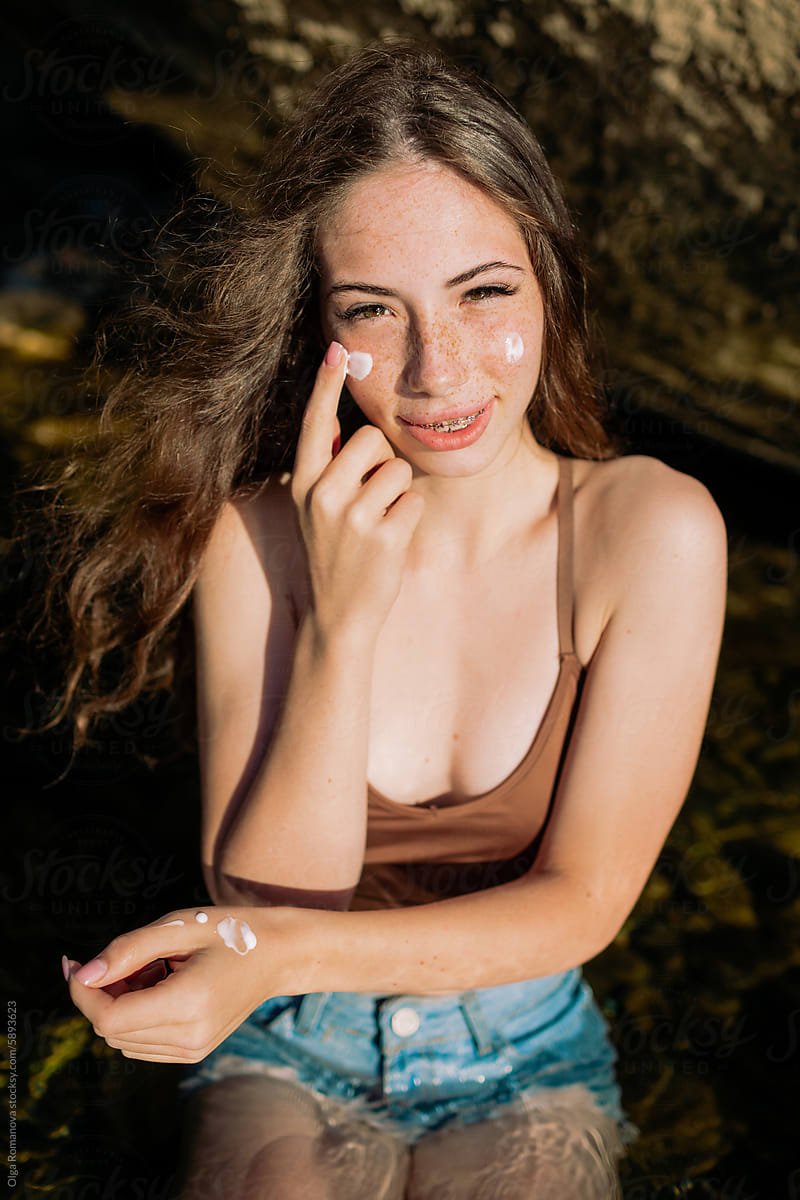 Summer portrait of happy teenage girl using sunscreen