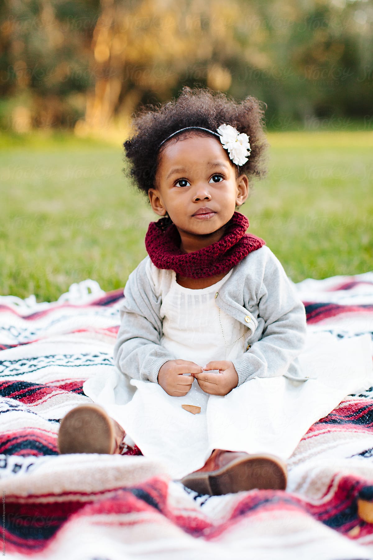 Beautiful little girl sitting on a blanket and looking up at her parents