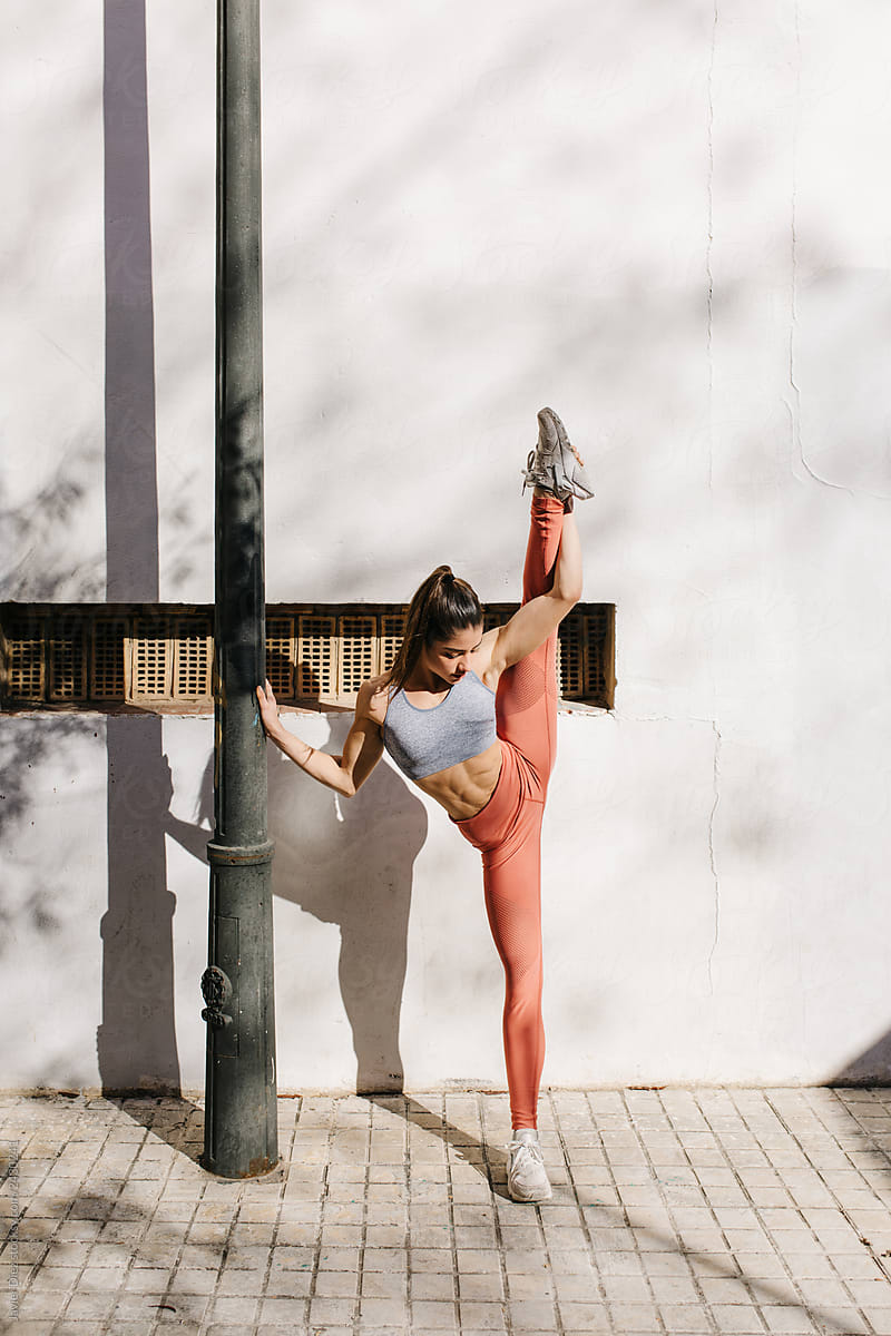 Young sportive woman stretching near grey wall