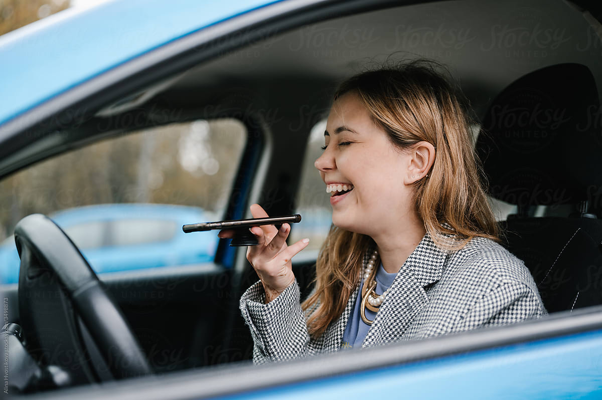 Cheerful woman recording voice message in car