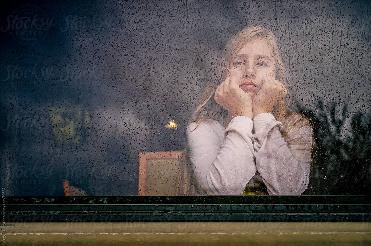 Girl looking out a window on a rainy day