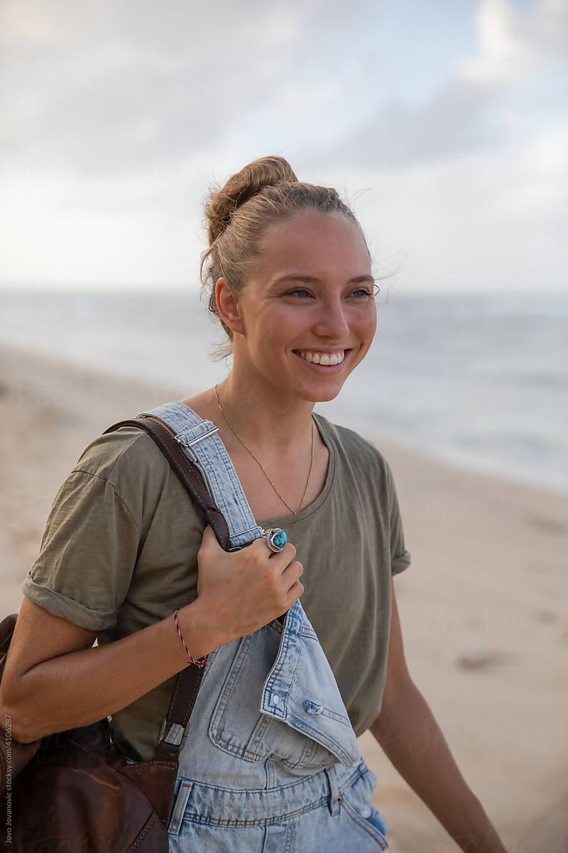 Smiling Woman Walking Down Beach Holding Bag
