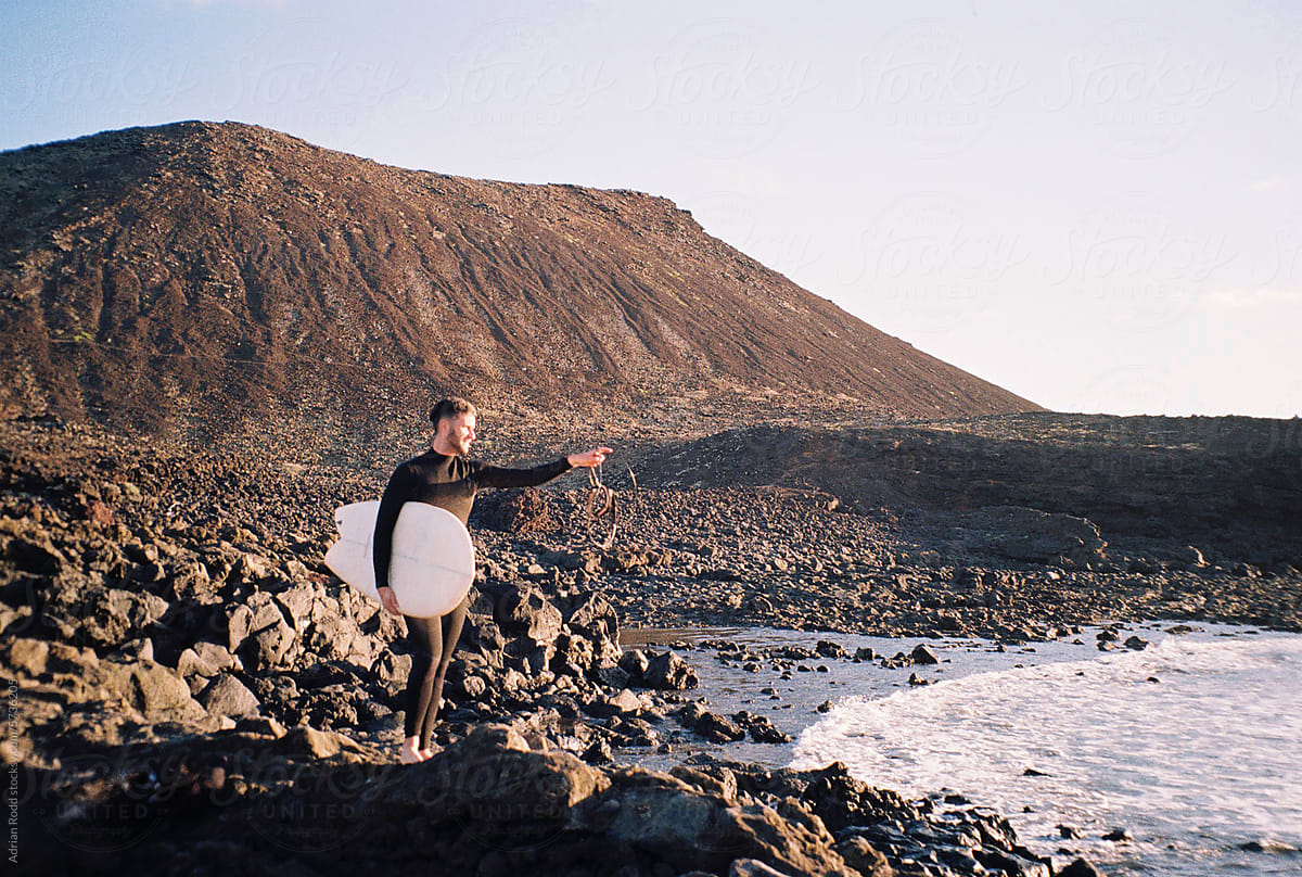 A young surfer gazes at the sea while standing on a rocky beach