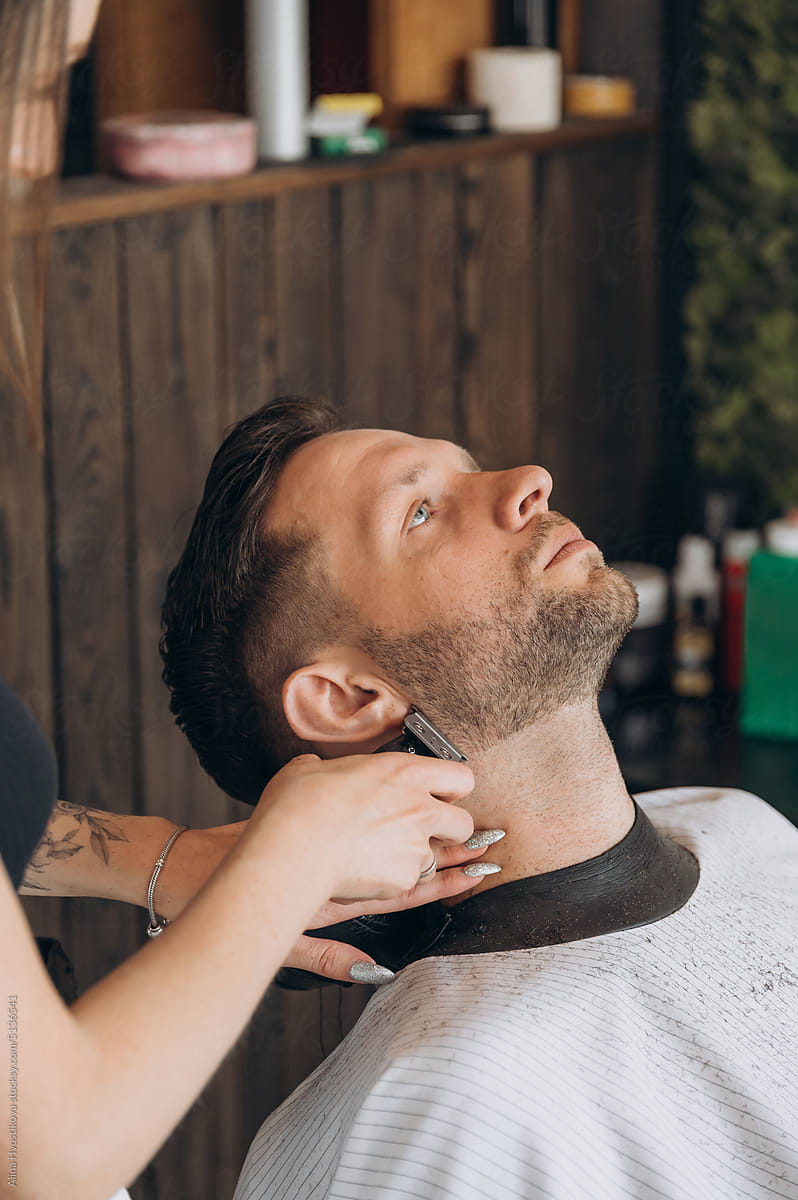 Crop tattooed barber trimming beard of client