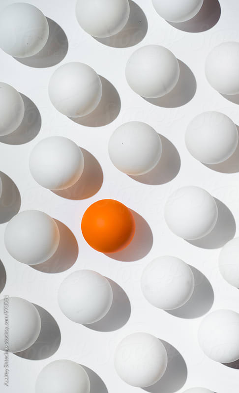 Orange ping pong balls surrounded with white balls one white background .