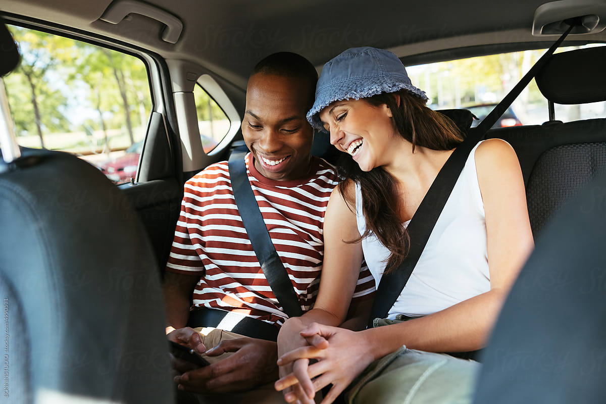 Positive couple browsing social media on back seat