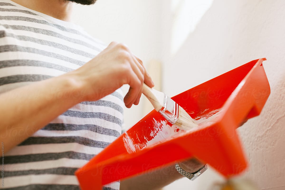 Young man painting a white wall in his new home with a brush.