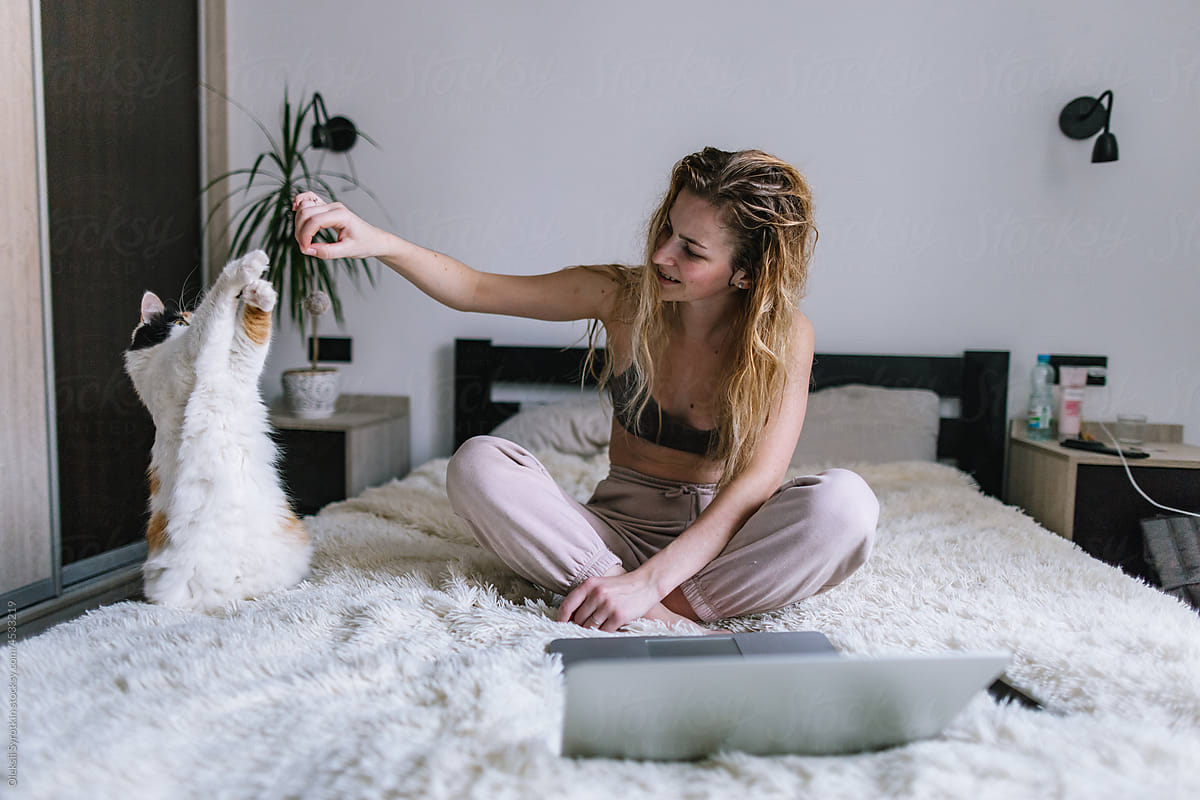 Woman spending time with cat on bed after distance work on laptop