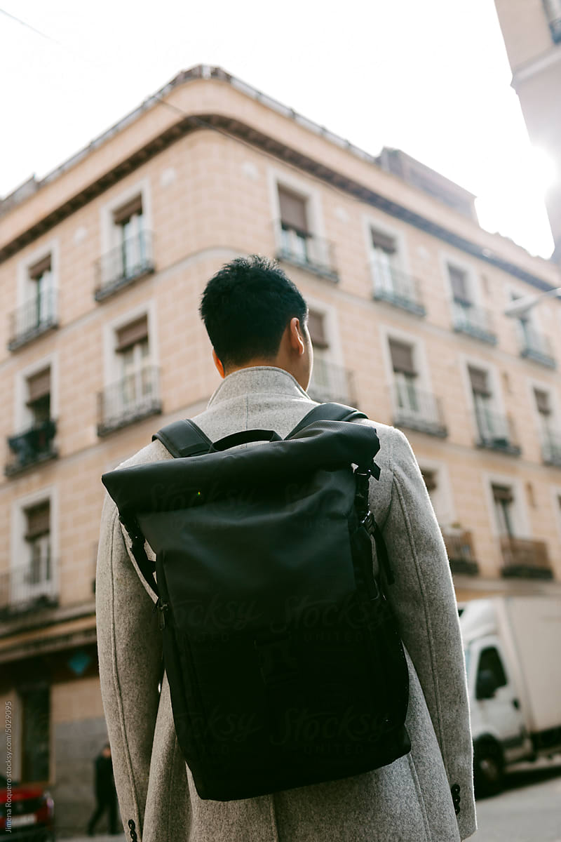 Back of young stylish man carrying a backpack in sunlight in the city