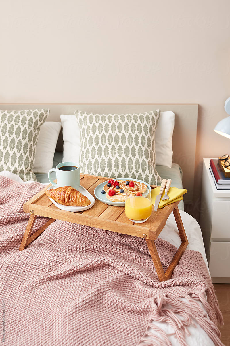 Cozy bed with wooden tray with continental breakfast.
