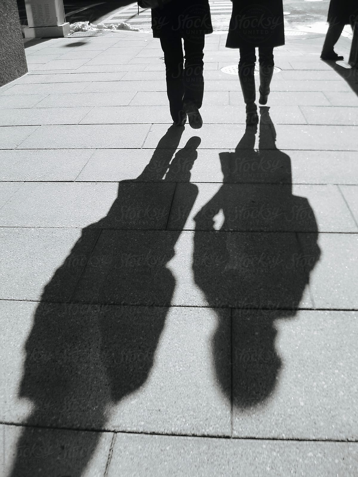 Pedestrians casting long shadows on urban sidewalk