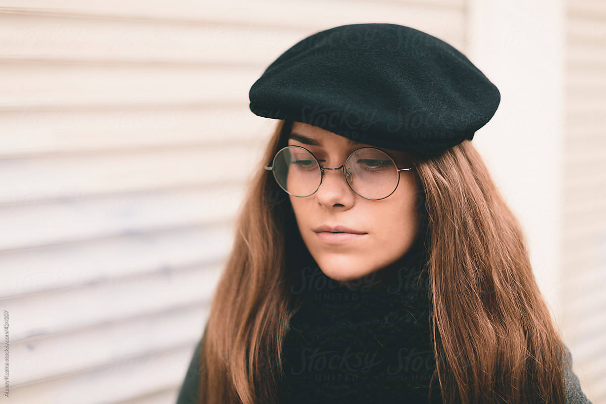 closeup of young woman with black hat and round glasses .