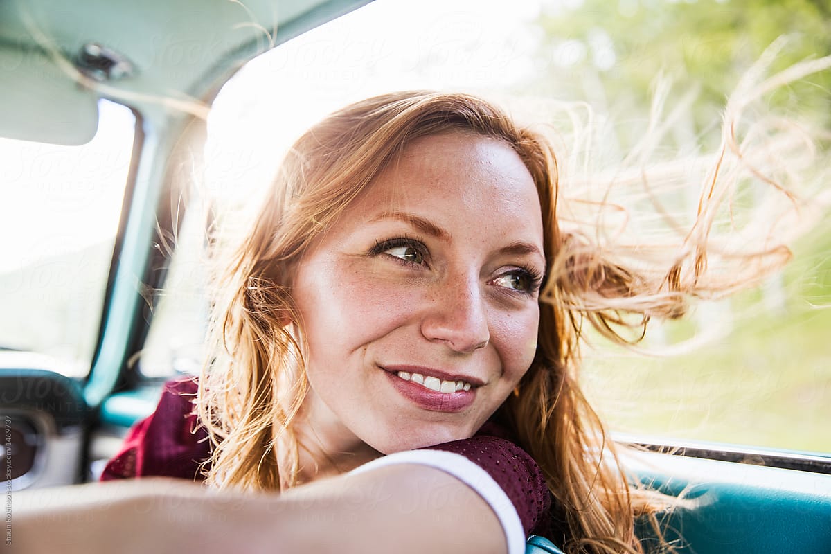 girl smiling behind her driving in a vintage car with her hair blowing in the wind.
