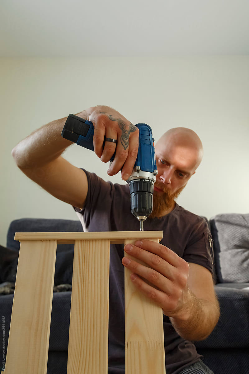Bearded guy assembling wooden shelf at home
