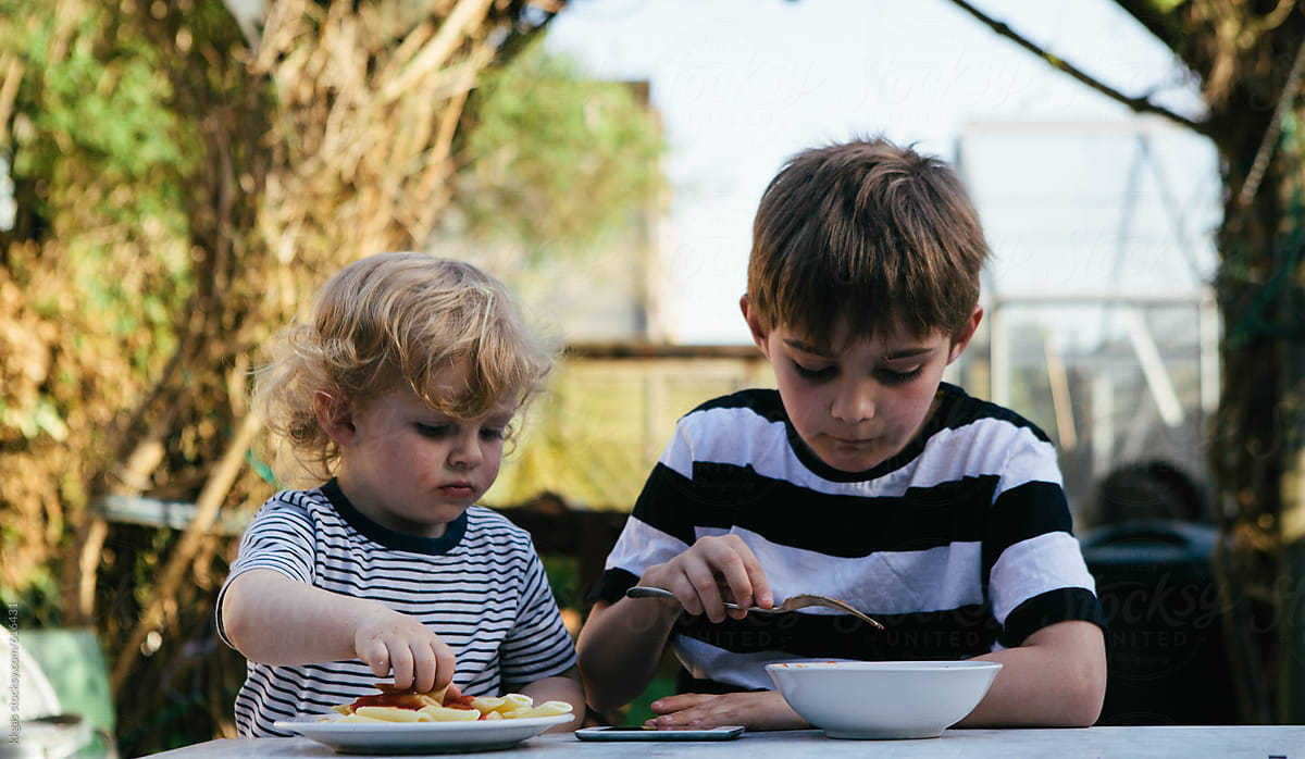 Two brothers eating pasta in a garden