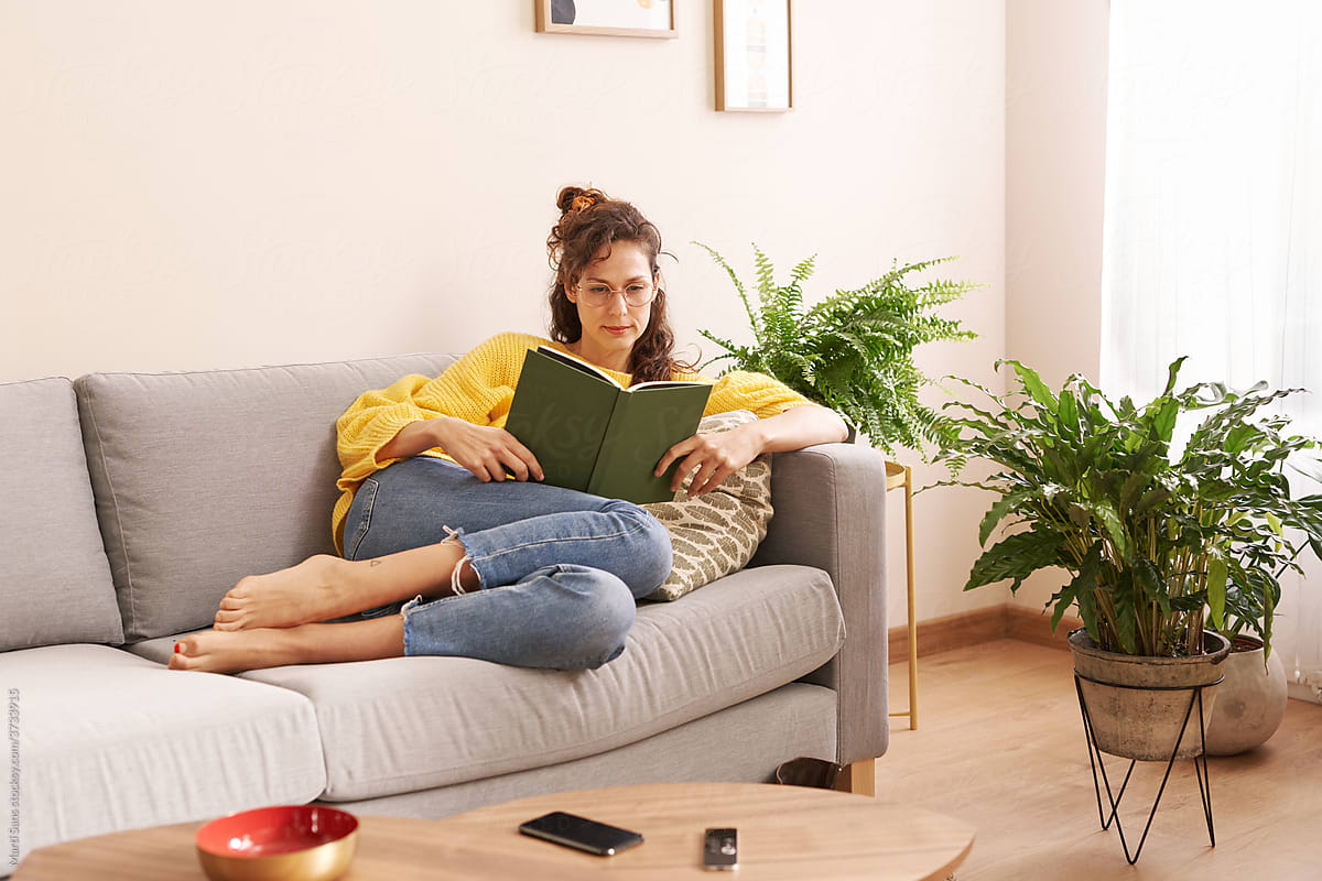 Thoughtful woman reading book in living room