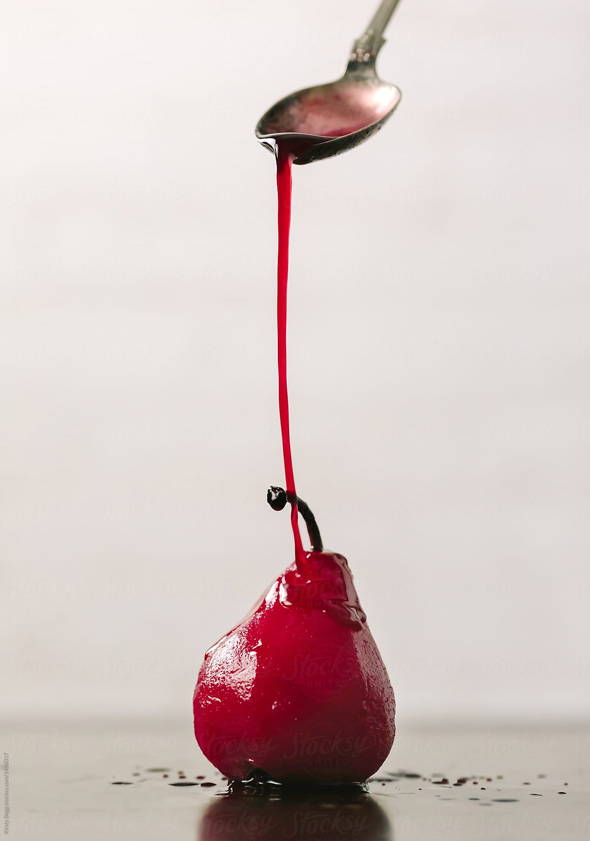Spoon drizzling red berry juice over poached pear