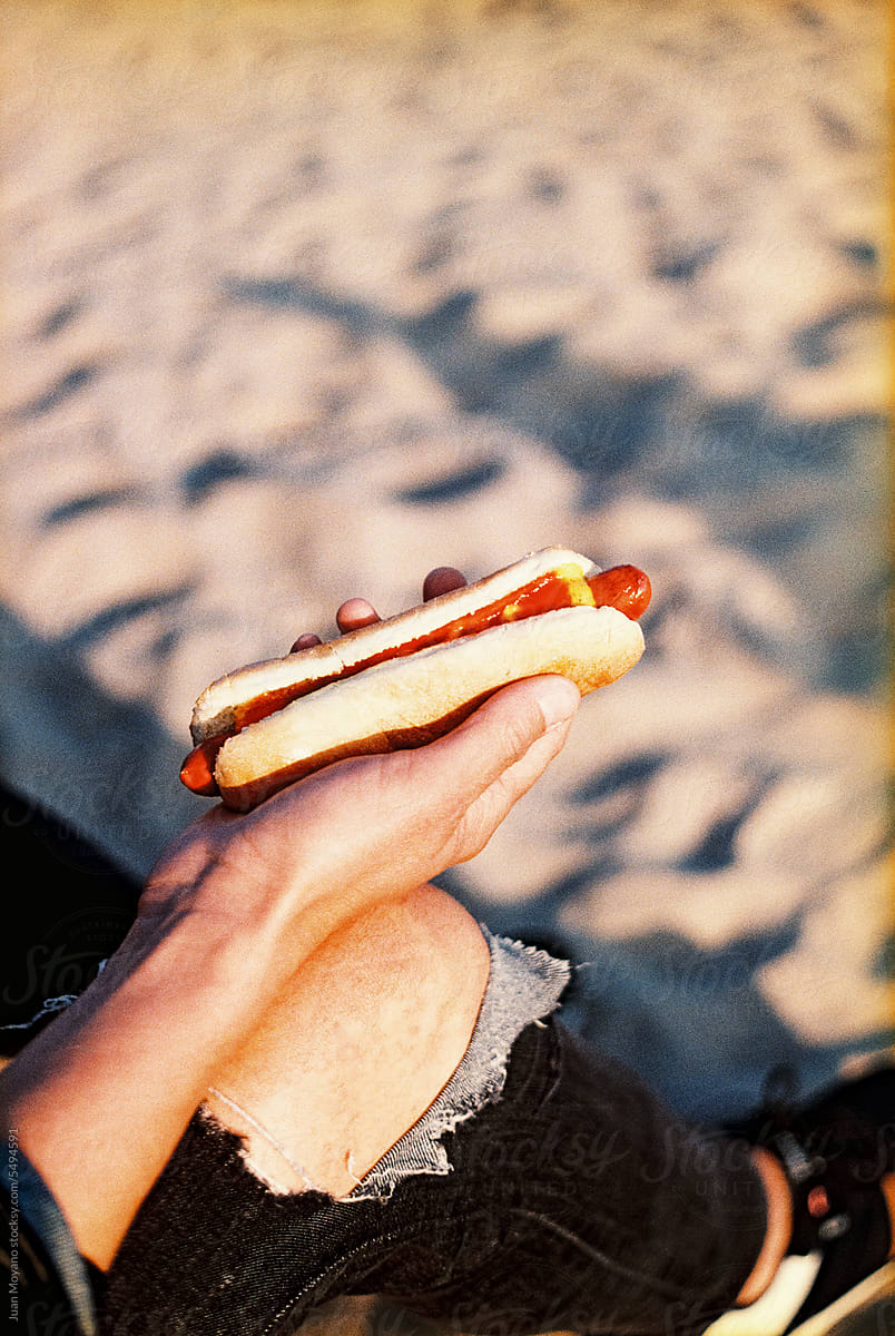 man holding a hotddog on the beach, 35 mm
