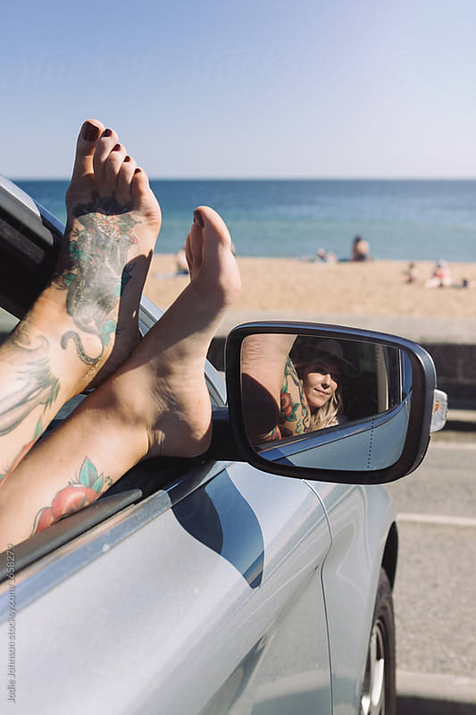 Female legs with tattoos hanging out the car window at the beach