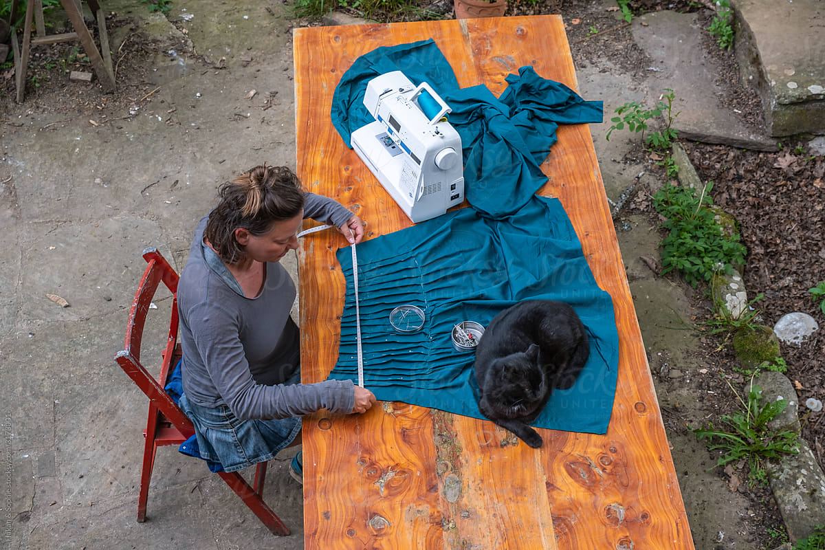 woman sewing in garden with black cat on the table