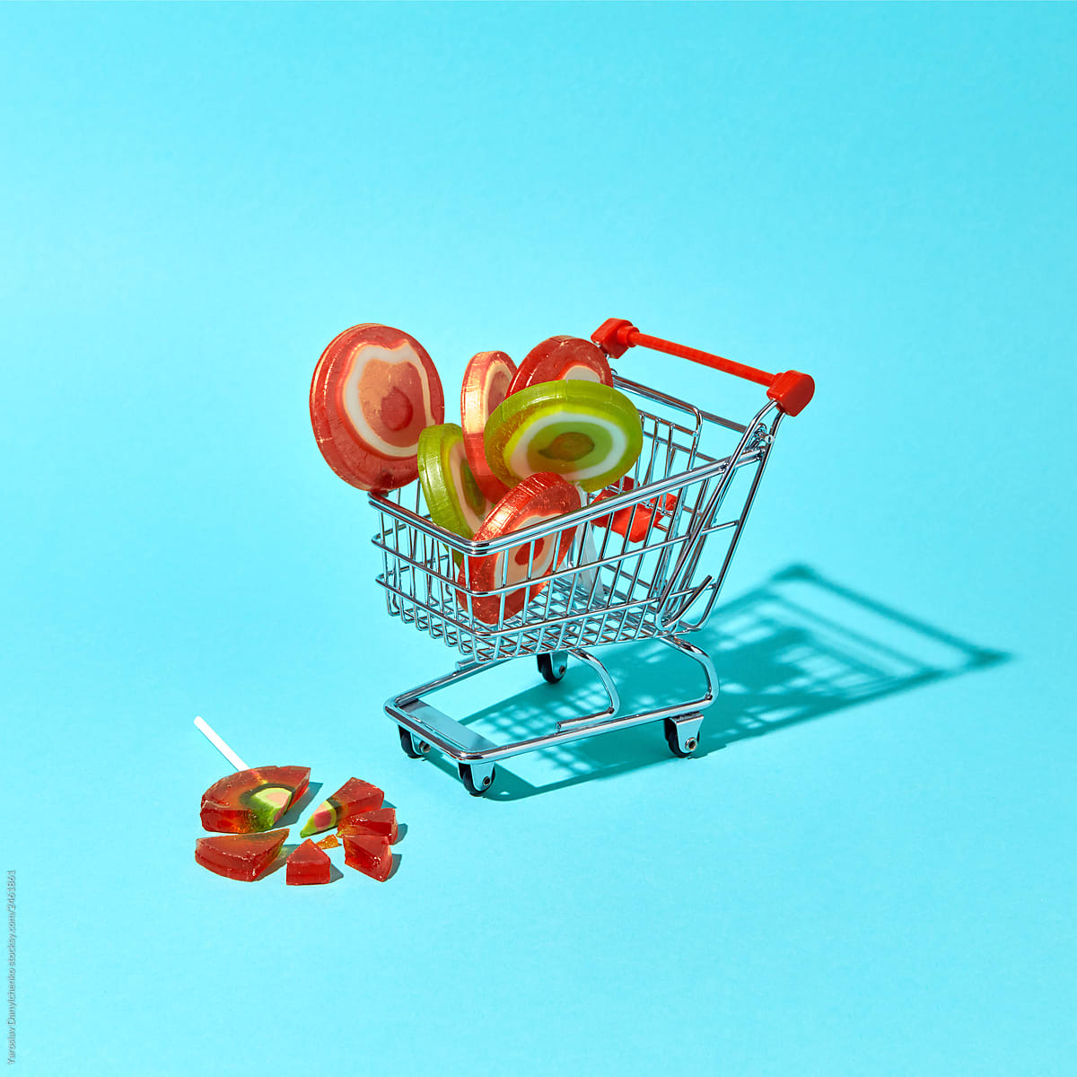 Shopping cart with different lollipops on a blue background with broken candy and copy space. Shopping concept