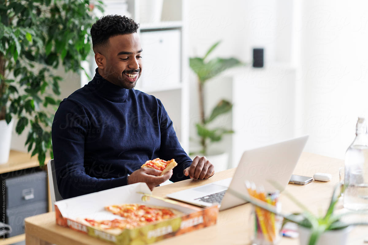 Smiling man eating pizza during remote work