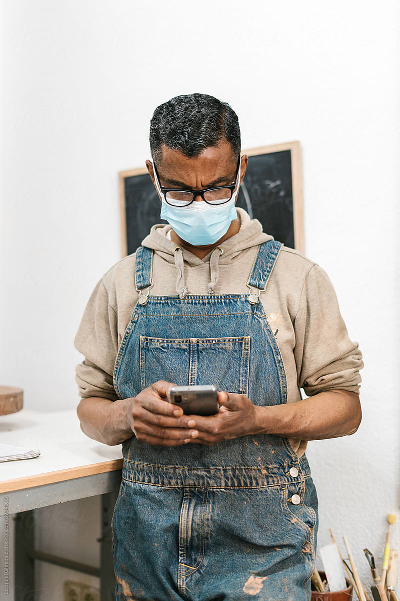 Black artisan using smartphone in pottery