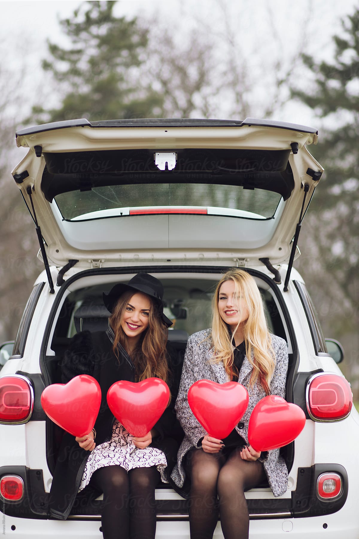 Two female friends holding heart shapped balloons for Valentine\'s day
