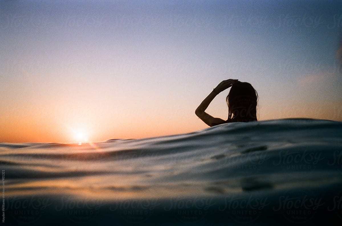 Girl Standing In An Ocean Wave Looking Out At A Beautiful Sunset By