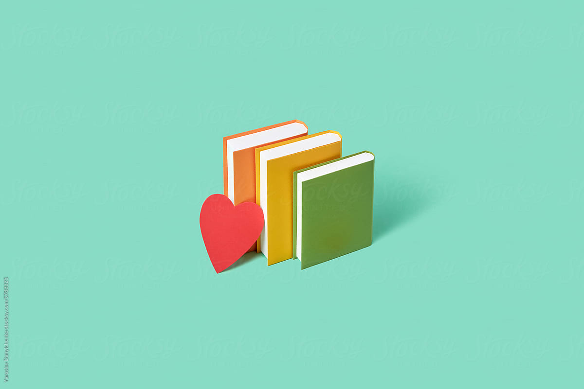 Red paper heart leaning on three books over pastel mint background