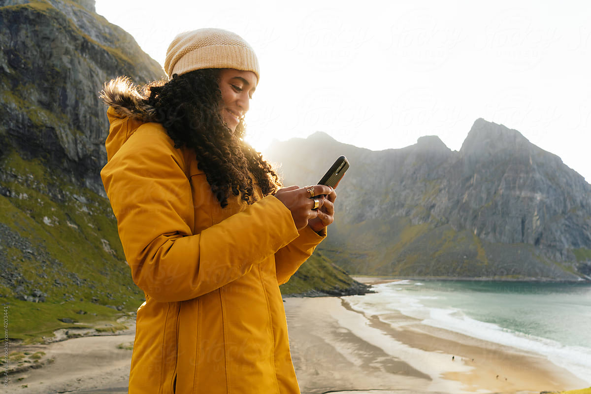 Cheerful woman browsing smartphone on seacoast