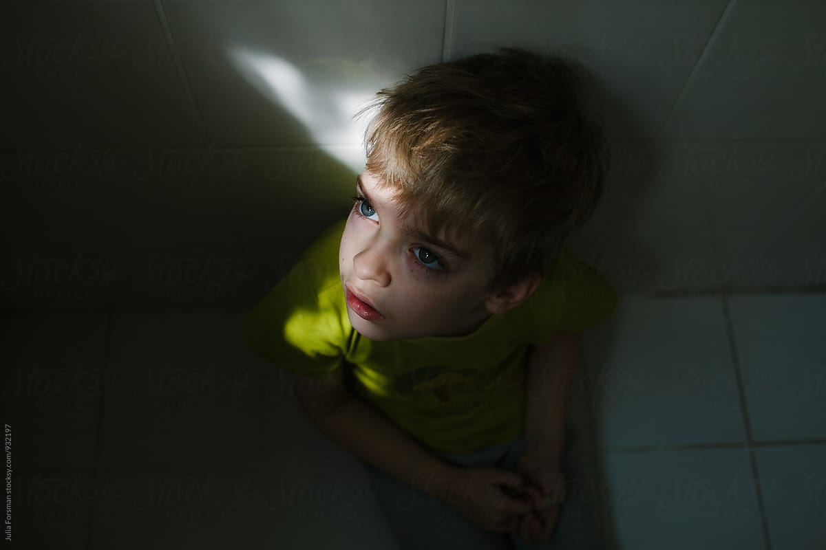 Boy sitting on bathroom floor with shaft of light on his face.