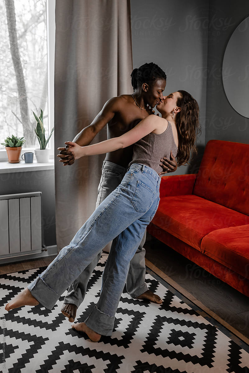 A loving interracial couple dances and kisses at home