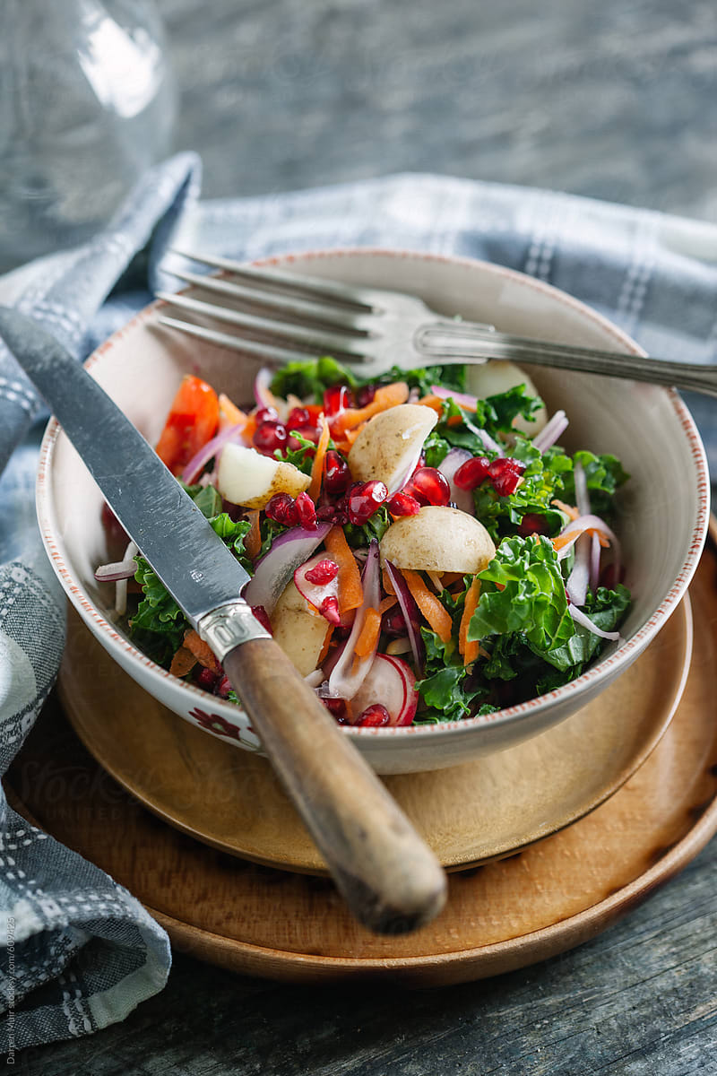 Healthy kale,potato and pomegranate salad on table with knife and fork.