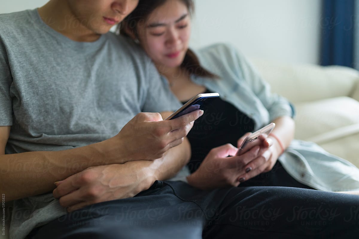 Young asian couple looking at mobile phone in home