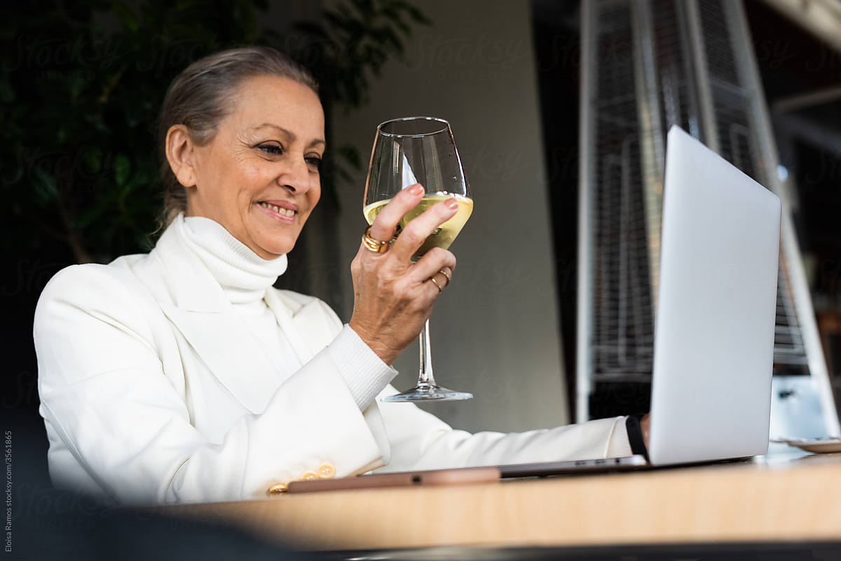 senior business woman on videoconference toasting with a cup of wine at restaurant