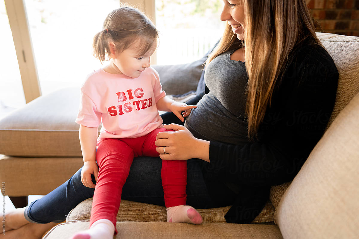 Cute girl in pink big sister shirt points to mother's pregnant belly