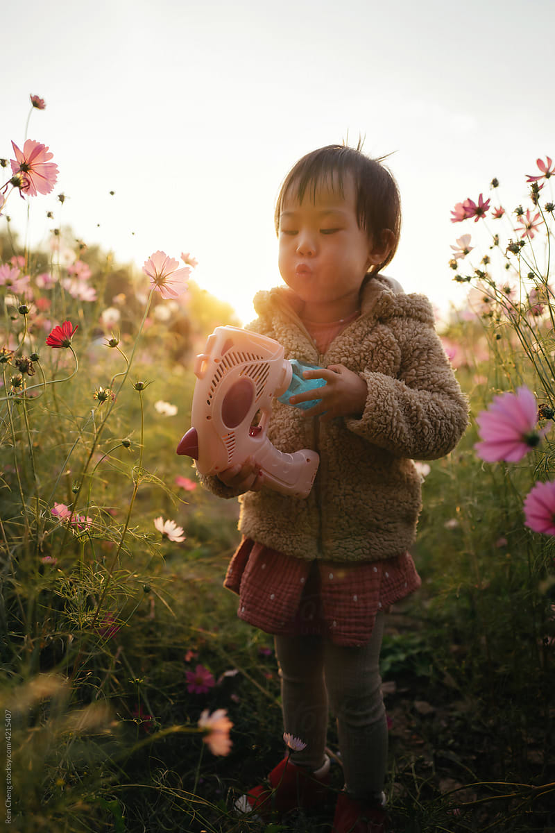 Baby playing with bubble machine in the flowers