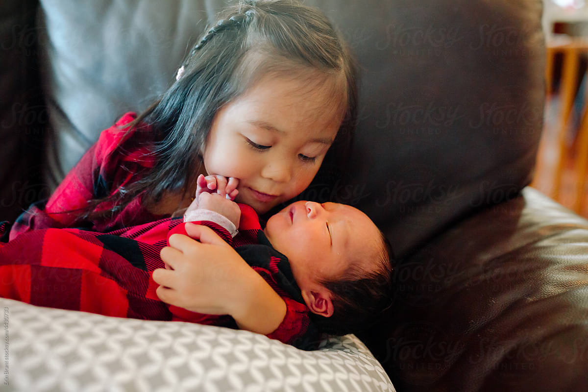 Little girl holding newborn brother in her arms