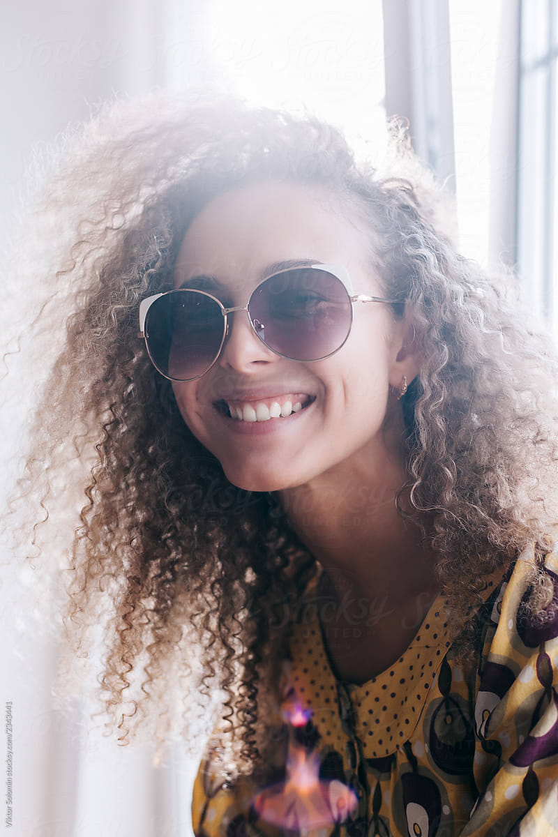 Indoor summer back light smiling happy portrait of young curly woman