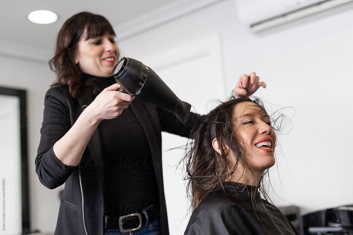 Shot of a cheerful hairdresser blow drying hair of a woman
