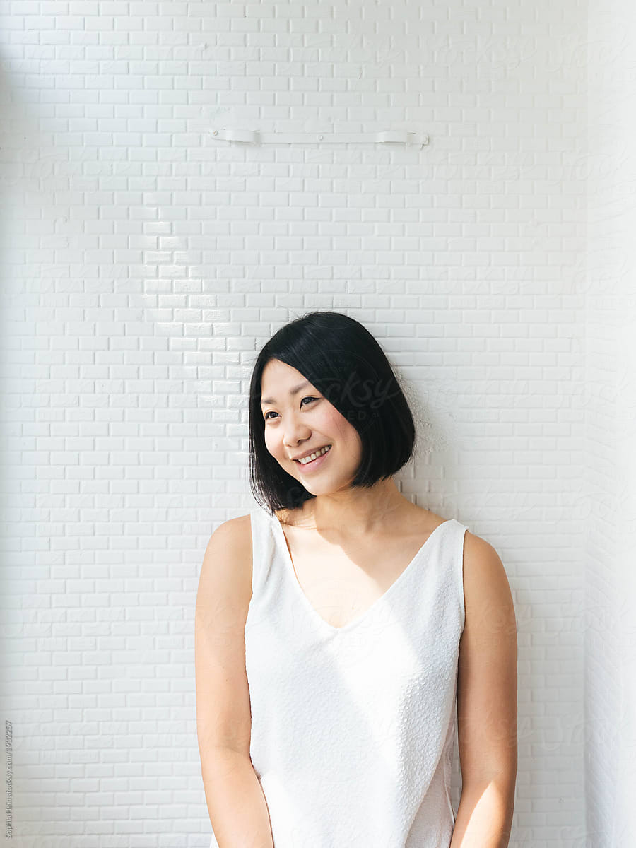 Minimalist portrait of joyful asian female with white background and sunlight